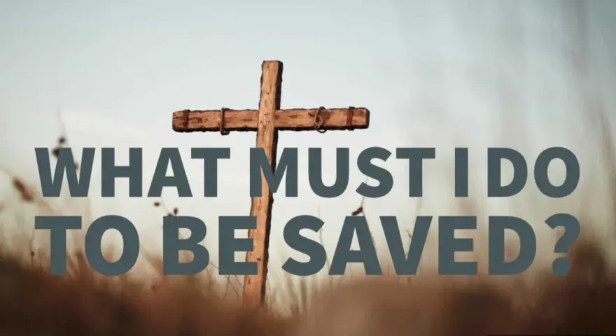 A wooden cross stands in a field of dry grass. Text reads: "WHAT MUST I DO TO BE SAVED?" This image explores the question of how to get to heaven.