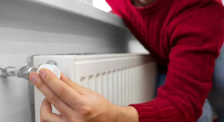 Mężczyzna w czerwonym swetrze reguluje termostat grzejnika, oszczędzając energię. To jego sposób na wykorzystanie bonu ciepłowniczy.