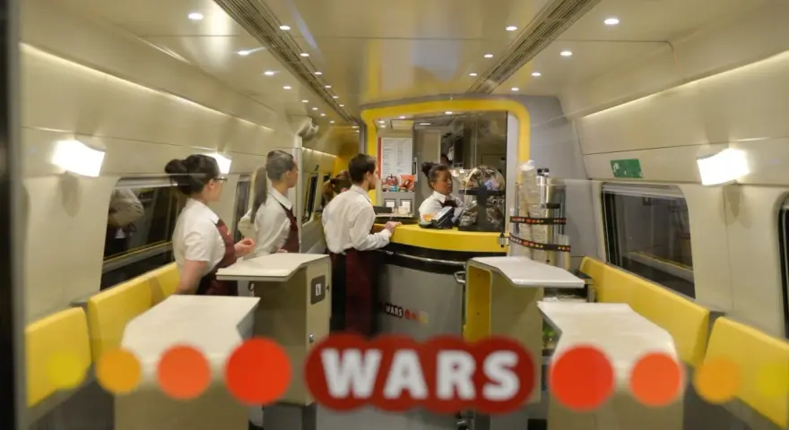 Wnętrze pociągu z personelem obsługującym bar. Widoczny napis "WARS".