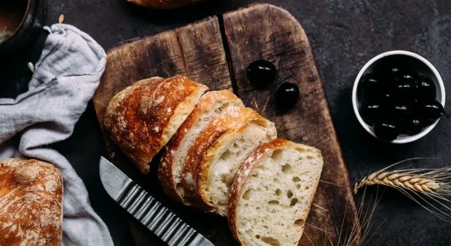 Frisches Brot, aufgeschnitten auf einem Holzbrett, daneben Oliven. Perfekt für den Gasgrill bei richtiger Temperatur.