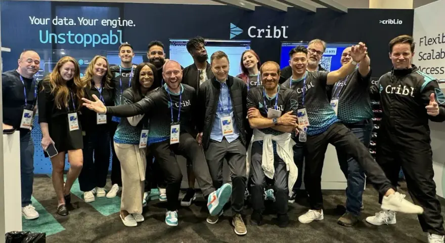 A lively group of Cribl customers and staff pose for a photo at a trade show, all smiles and team spirit.