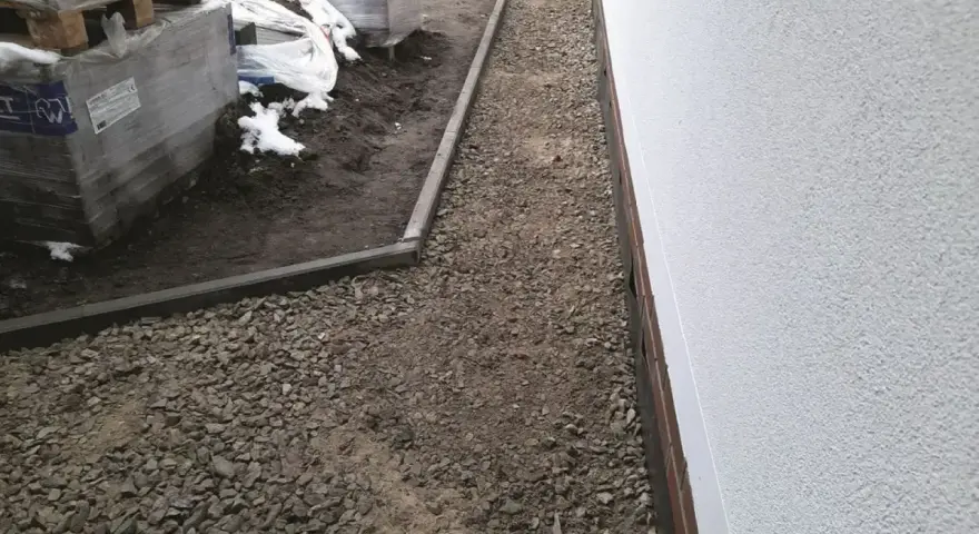 Wykonano opaskę wokół domu z kruszywa, obok ułożone palety z materiałami budowlanymi.
