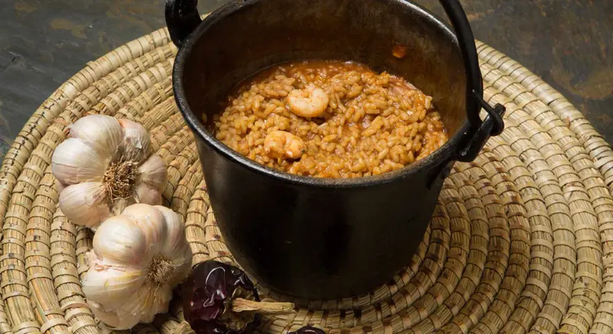 Caldero murciano humeante en olla de hierro, con gambas, ajos y pimientos secos.