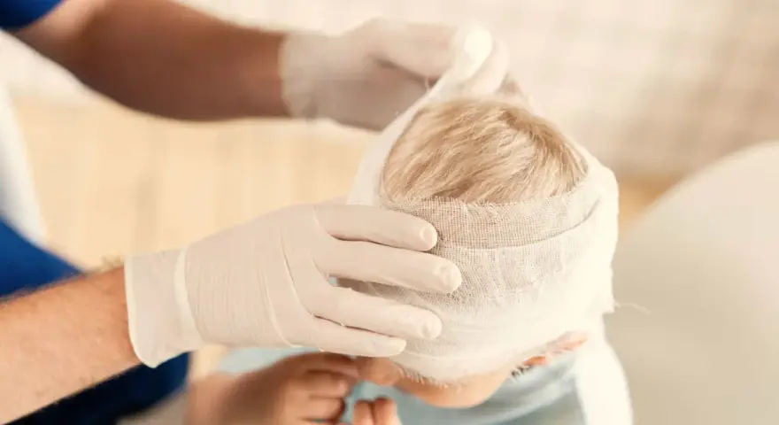 Manos enguantadas vendan la cabeza de un niño, curando sus heridas.
