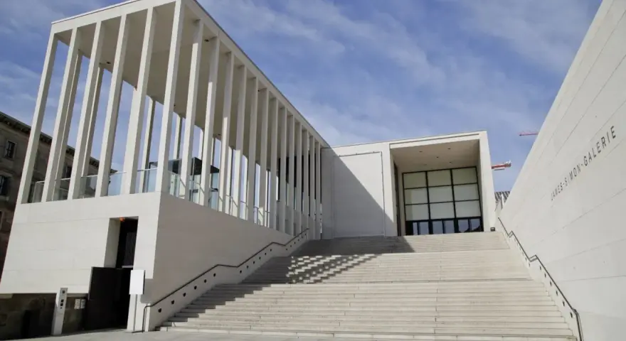 Moderne berlin architektur: James-Simon-Galerie mit langer Treppe und Säulengang vor blauem Himmel.