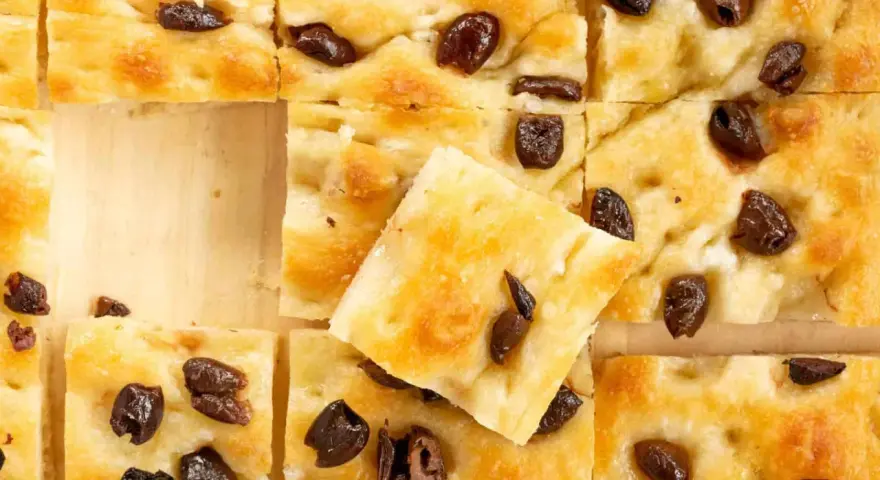 Goldbraune Focaccia mit Oliven, perfekt nach dem original focaccia rezept. Ein Stück ist leicht angehoben.