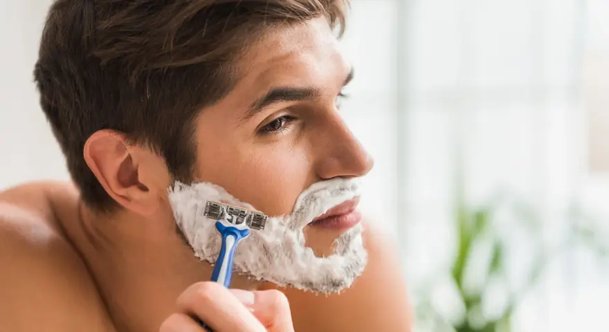 Hombre afeitándose la barba con espuma y maquinilla. La espuma de afeitar sirve para lubricar y proteger la piel.