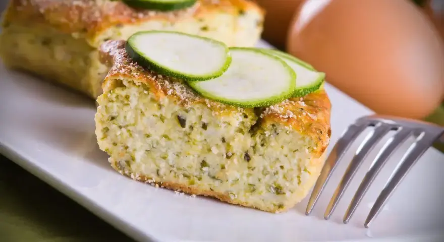 Saporito sformato di zucchine, guarnito con fette di zucchina fresca e una spolverata di parmigiano. Perfetto per un pasto leggero.