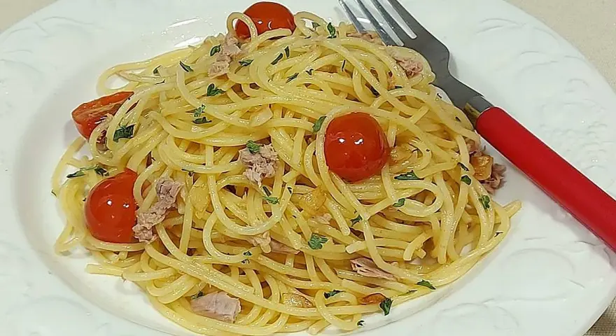 Espaguetis al ajillo con tomates cherry y atún, servidos en plato blanco con tenedor rojo.
