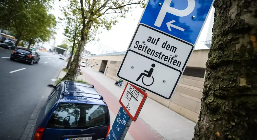 Schild für Behindertenparkplatz auf dem Seitenstreifen. Falschparken wird mit einer hohen Strafe geahndet.