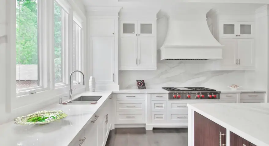 Cocina blanca moderna con encimeras de mármol, campana extractora y estufa profesional.