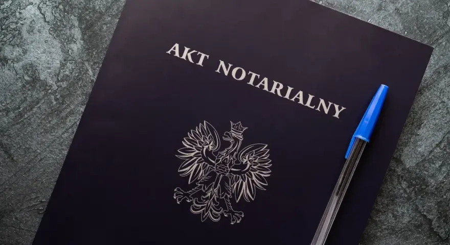 Na ciemnogranatowej okładce widnieje napis "AKT NOTARIALNY" i godło Polski. Obok leży niebieski długopis.