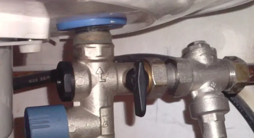 Un réducteur de pression, comme ce dispositif métallique avec une poignée noire, sert à réguler la pression de l'eau dans une installation.