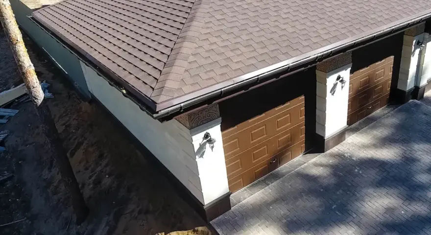 Nowy dach papa na garażu z brązowymi drzwiami i ozdobnymi słupkami.