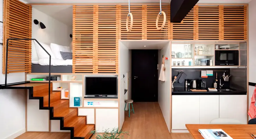 Estudio moderno de piso 25 metros cuadrados con cama elevada, cocina compacta, zona de TV y escaleras de madera.