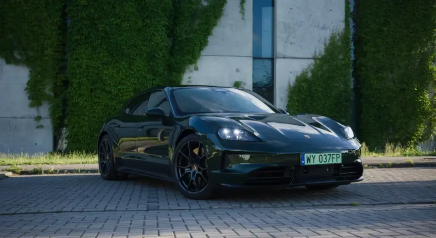Elegancki, ciemnozielony Porsche Taycan na tle zielonej ściany z bluszczu. Sprawdź aktualną porsche taycan cena i możliwości tego elektrycznego cudu.