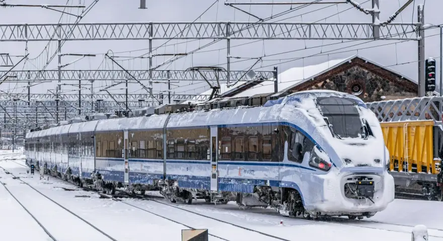 Pociąg PKP Intercity pokryty lodem i śniegiem, stojący na zaśnieżonych torach. Utrudnienia w ruchu kolejowym z powodu zimy.
