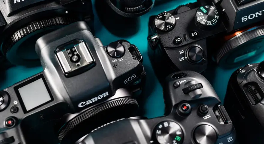 Zbliżenie na kilka aparatów cyfrowych marek Nikon, Canon i Sony ułożonych na niebieskim tle.