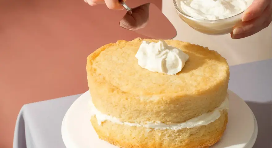 Nakładanie puszystego kremu na biszkoptowe ciasto z mascarpone.