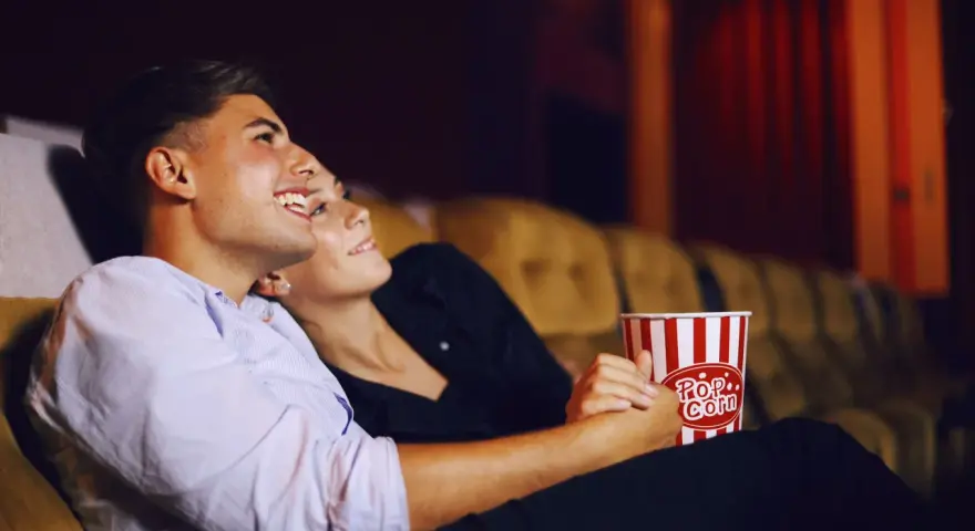 Para randkę do kina wybierz wygodny, ale stylowy strój. Para siedzi blisko siebie, trzymając popcorn.