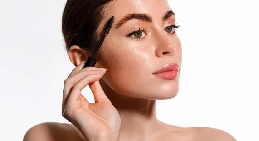 Une femme applique un mascara pour un maquillage des yeux parfait. Ses sourcils sont brossés et ses cils sont mis en valeur.