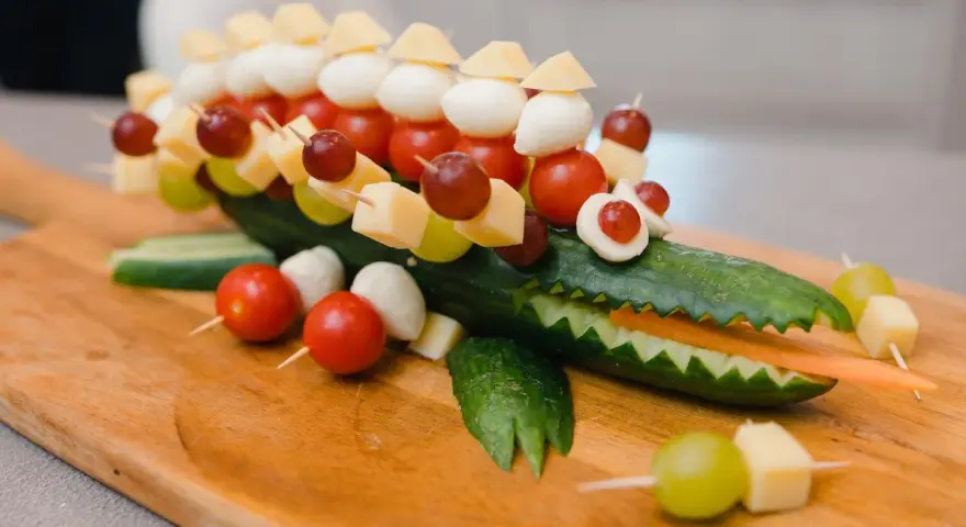 Krokodil aus Gurke mit herzhaftem Fingerfood für Kinder: Käse, Tomaten, Mozzarella & Trauben auf Spießen.