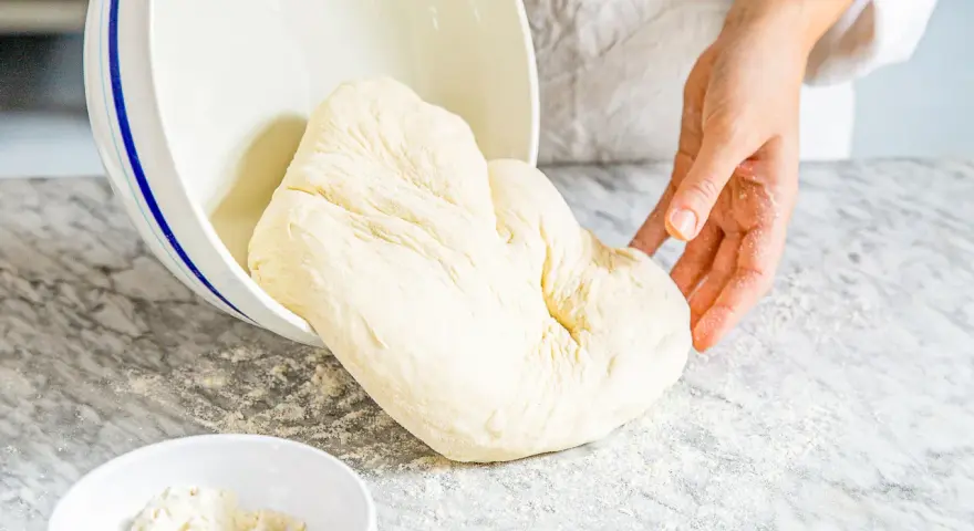 Frischer Teig, der aus einer Schüssel auf eine bemehlte Arbeitsfläche gleitet. Ähnlich wie Mehl Typ 0, ideal zum Backen.