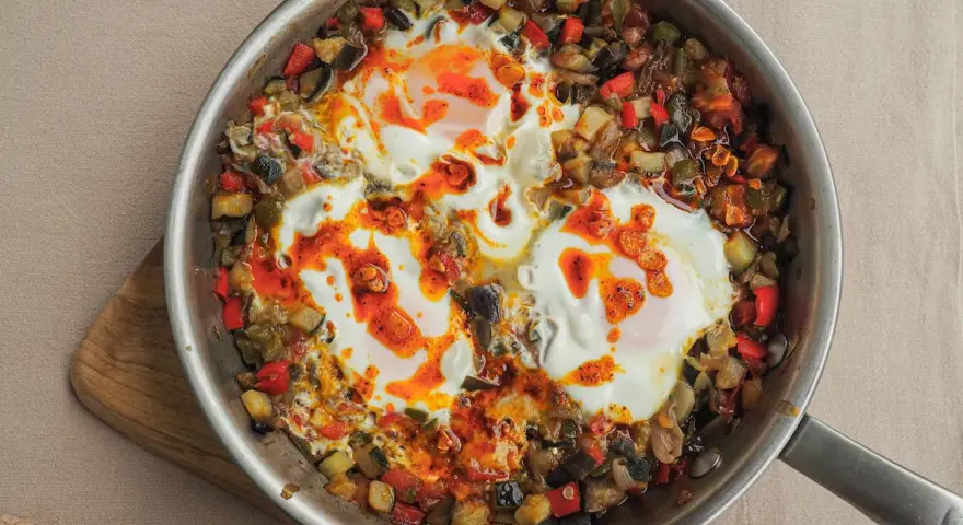 Huevos al plato con verduras salteadas, pimientos, calabacín y berenjena, todo en una sartén.