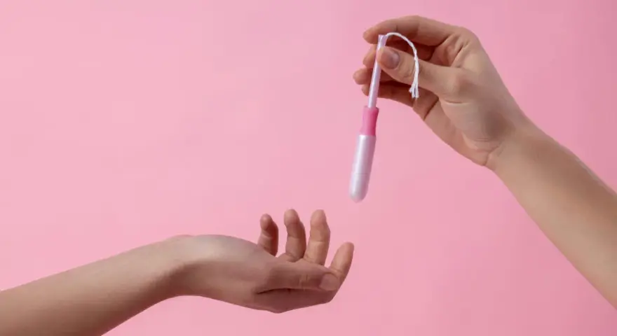 Dwie dłonie, jedna trzyma tampon z aplikatorem, druga wyciągnięta do przyjęcia. Ciasna pochwa to temat, który wymaga dyskrecji.