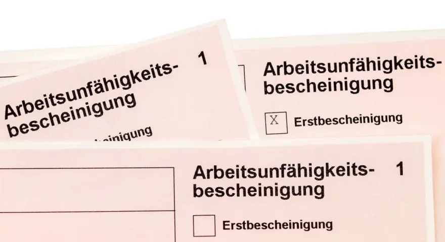 Arbeitsunfall krankschreibung unterbrochen: Mehrere Arbeitsunfähigkeitsbescheinigungen liegen übereinander. Eine Folgebescheinigung ist angekreuzt.