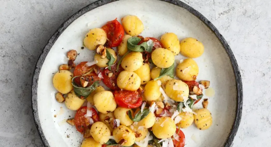 Gnocchi z pomidorkami koktajlowymi, szałwią i orzechami laskowymi, posypane parmezanem. Pyszne danie na obiad.