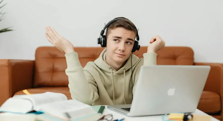 Chłopak w słuchawkach z laptopem przed sobą, z książkami i notatkami. Może to być jego przygoda z kształceniem słuchu online.