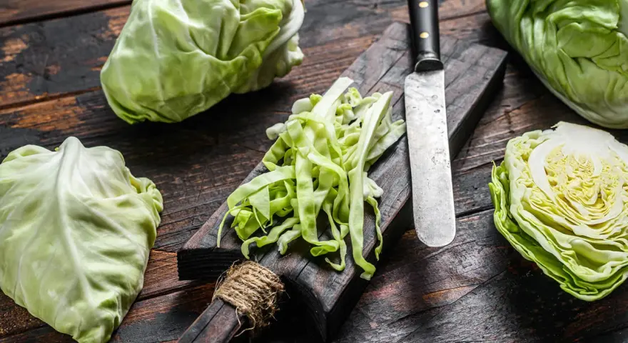 Frischer spitzkohl schneiden für einen Salat. Ein Messer liegt neben dem geschnittenen Kohl auf einem Holzbrett.