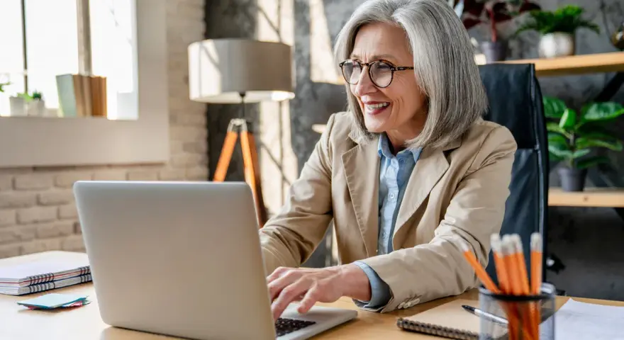 Femme souriante travaillant sur son ordinateur portable, planifiant sa future pension pré cheval.