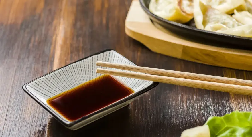 Sos sojowy w miseczce z pałeczkami, obok pierożków gyoza. Szukasz alternatywy, czym zastąpić sos sojowy?