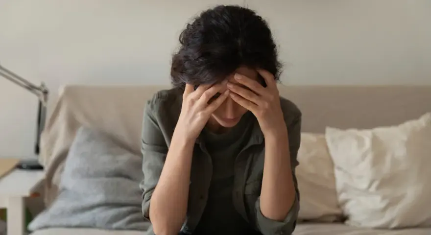 A woman sits with her head in her hands, overwhelmed by the cycle of self-destruction.