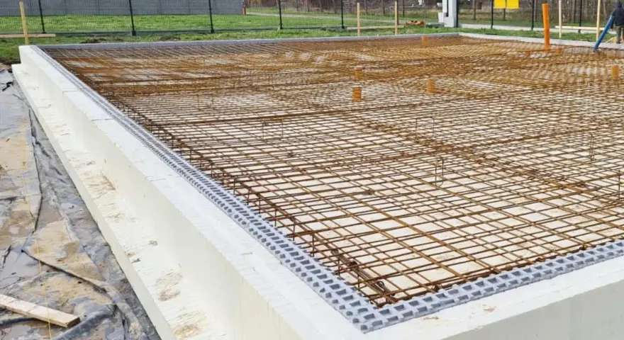 Siatka zbrojenia na fundamencie z białych bloczków styropianowych, gotowa do zalania betonem.