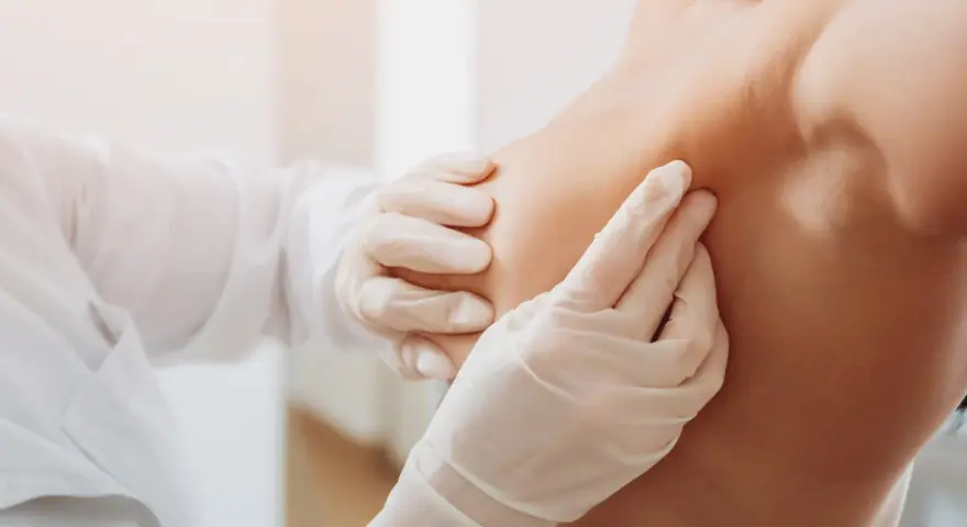 Arzt in Handschuhen tastet Brust ab.