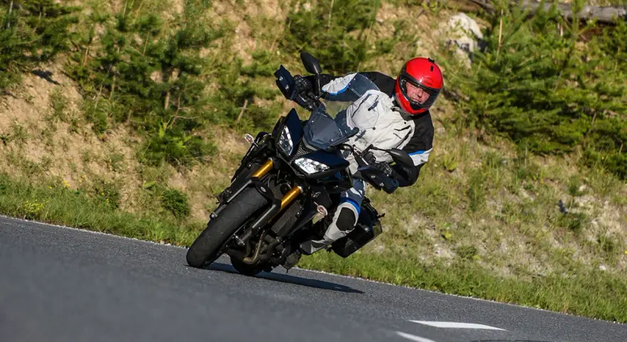 Motocyklista w kasku na zakręcie górskiej drogi. Planujesz podróż na Korsykę? Sprawdź ceny paliwa i noclegów!