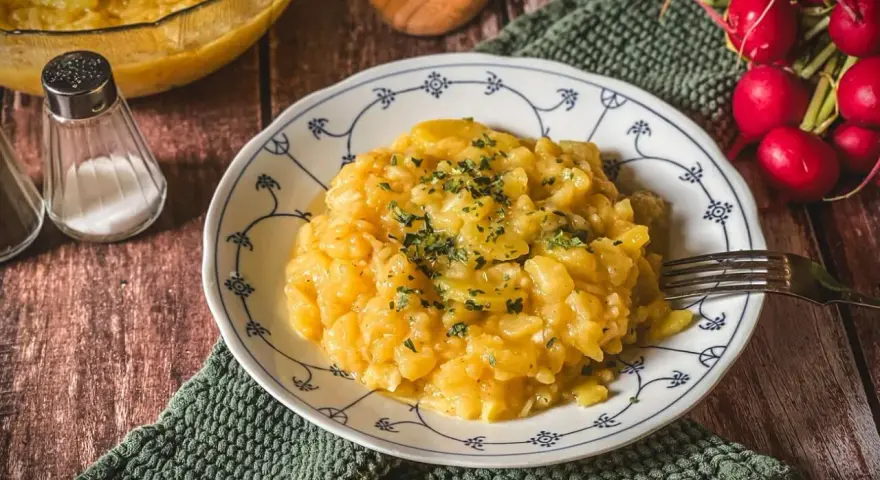 Omas Kartoffelsalat, ein Klassiker auf dem Holztisch, garniert mit Petersilie. Daneben Radieschen und Salzstreuer.