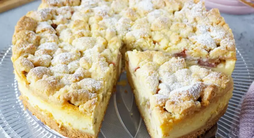 Ein saftiger Rhabarberkuchen mit Puddingfüllung und Streuseln, bestäubt mit Puderzucker.