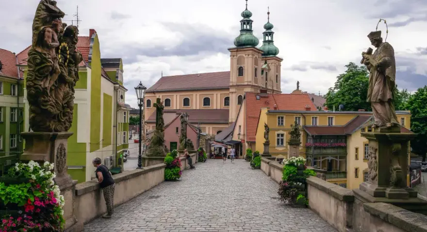 Kamienna, brukowana ścieżka prowadzi do barokowego kościoła z zielonymi wieżami. Wzdłuż mostu stoją kamienne rzeźby. To piękne ziemia kłodzka atrakcje.