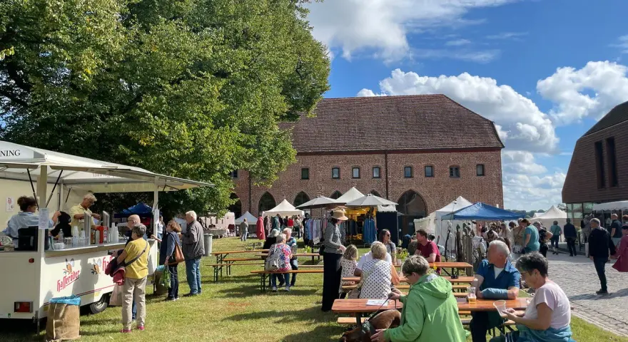 Sommerliche Zarrentin Veranstaltungen: Menschen genießen ein Fest mit Ständen und Sitzgelegenheiten im Freien vor historischen Gebäuden.