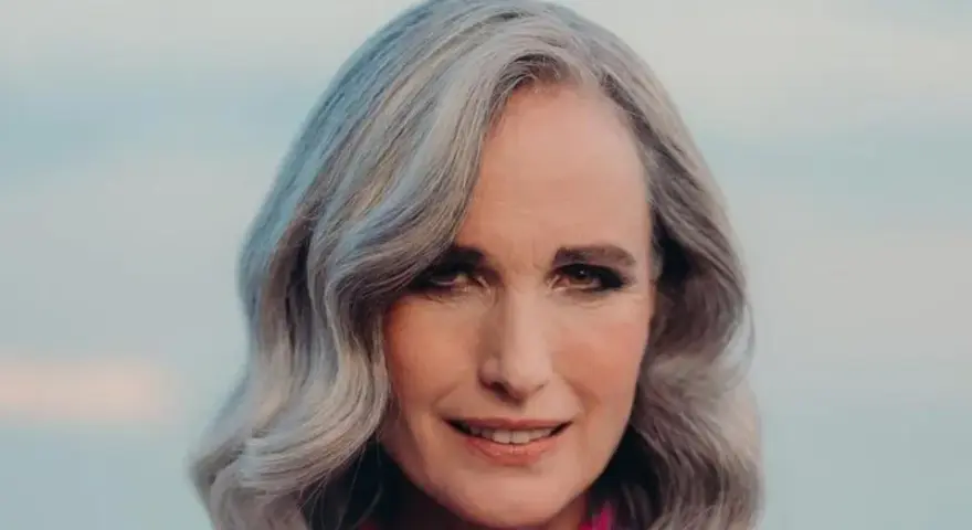 Mujer de 50 años con cabello plateado y ondulado, sonriendo suavemente. Se aprecian las líneas de expresión, reflejo de la flacidez facial a los 50.