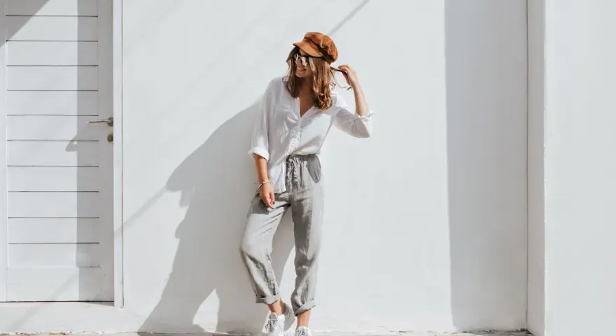 Modello con cappello marrone e occhiali da sole, indossa una camicia bianca e pantaloni grigi. Un esempio di abbinamenti outfit grigio casual e chic.