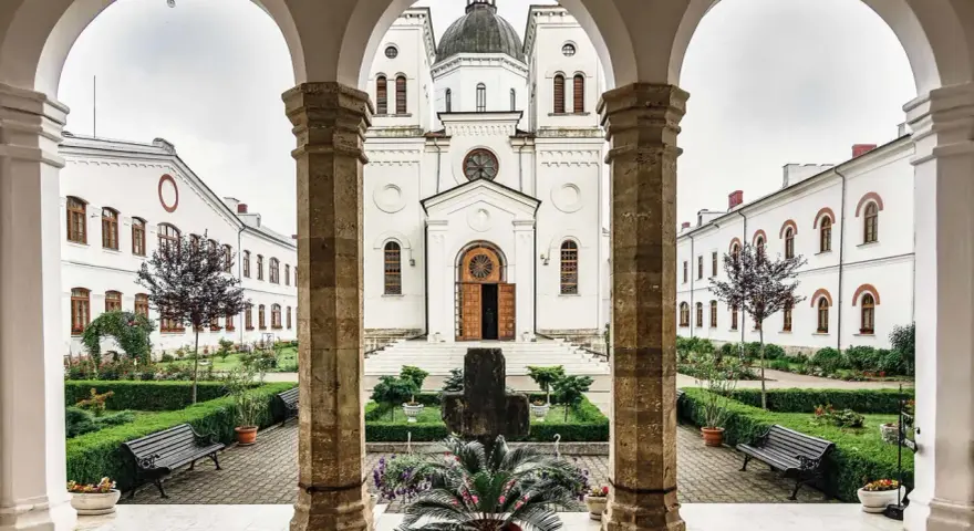 A courtyard with a cross and potted plants, framed by arches. The white church in the background is a place where monks like Father John and Brother Michael find peace.