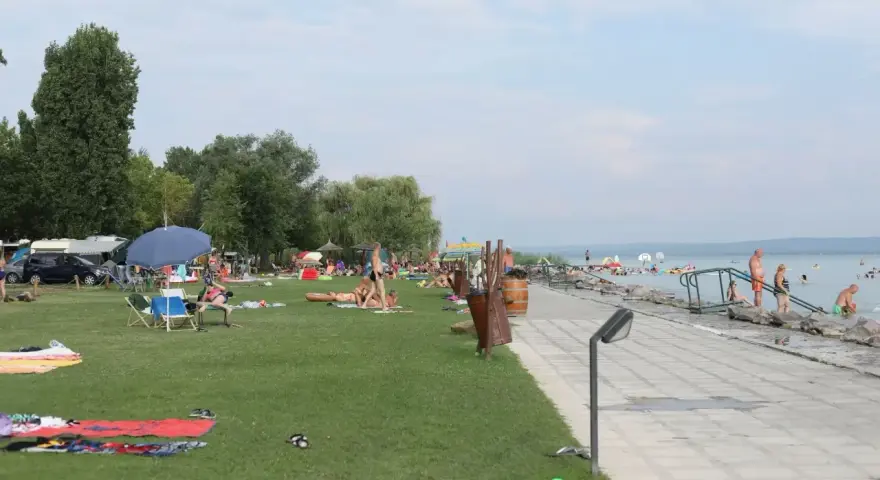 Ludzie odpoczywają na plaży i w wodzie. W tle widać kampery, co sugeruje, że to popularne miejsce na napfeny camping.