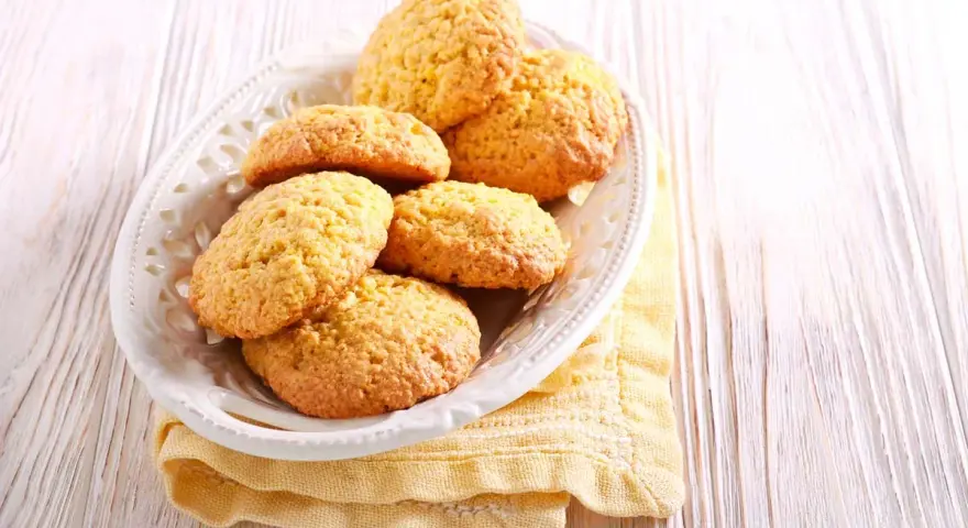 Biscotti con farina di mais dorati e friabili, serviti in un piatto bianco su un tovagliolo giallo.