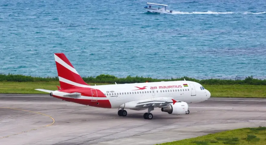 Samolot Air Mauritius na pasie startowym, w tle turkusowe morze i łódź. Twoje loty na Mauritius właśnie się zaczynają!