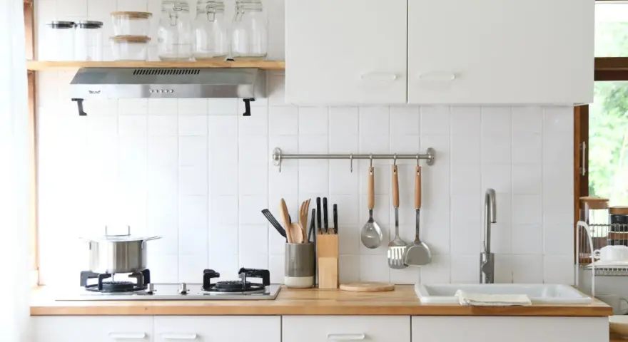 Diseños de cocinas pequeñas y sencillas: encimera de madera, campana extractora, utensilios colgados y un fregadero blanco.